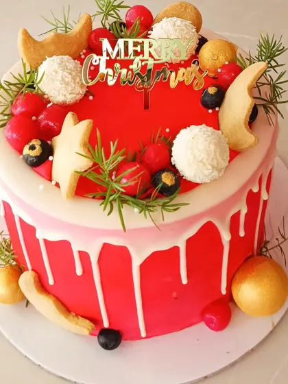 A bright and cheerful red drip cake for Christmas, decorated with cookies, cherries, and festive greens.