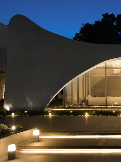 A close-up of the signature architectural curve of "The Rising Wave" at night. The upward sweep of the concrete shell is accentuated by carefully placed lighting, turning the structure into a dramatic sculpture.