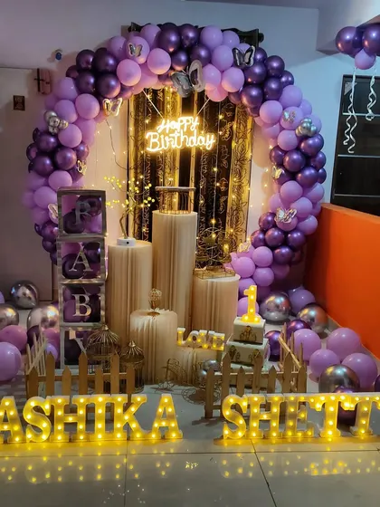 A beautiful purple and silver themed birthday party. This full setup includes a circular balloon arch, 'BABY' blocks, a picket fence, and large marquee letters for the name.