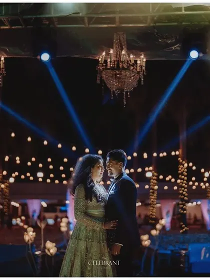 A romantic shot of a couple under grand chandeliers and spotlights at their outdoor reception.