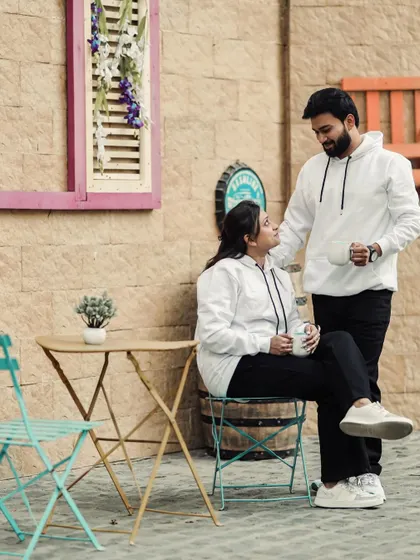 A casual and sweet pre-wedding shot of a couple in matching hoodies, enjoying a coffee date at a cafe-style studio set.