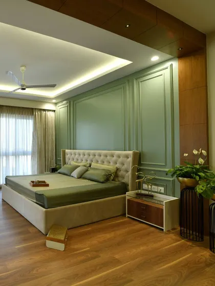 A wide view of the master bedroom, showcasing the grand feel created by the green wainscoting, veneer archway, and suede-finished bed. The layered lighting and wooden floors add warmth and sophistication.