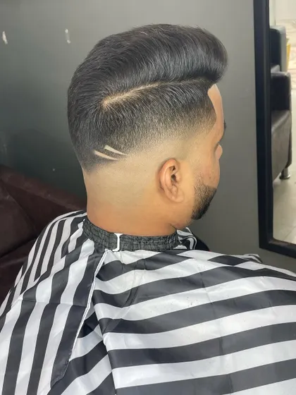 A side-back angle of a high-volume haircut with a skin fade. The small, clean line design adds a touch of personality to the style.
