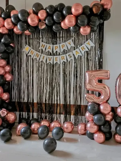 A 50th-anniversary decoration with a black and rose gold balloon arch, a shimmer curtain, and large '50' foil balloons.