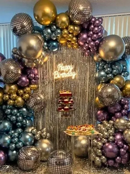 A retro disco theme perfect for an adult birthday party. This decoration is built around a silver fringe curtain and an arch of chrome and metallic balloons, with disco balls scattered throughout for a fun, party vibe.