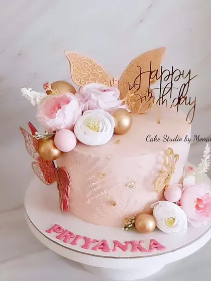 A beautiful floral cake made without any fondant. This design features a soft pink buttercream base, adorned with flowers, butterflies, and gold spheres for a touch of glamour.