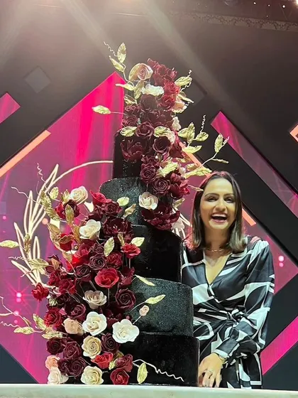 A moment of pure joy next to a dramatic, five-tiered black wedding cake adorned with a cascade of red, burgundy, and gold sugar flowers. I love creating bold, unforgettable designs like this one.