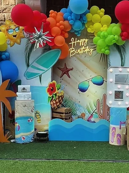 A close-up of the vibrant pool party backdrop, featuring a 'Happy Birthday' neon sign, surfboards, and sunglasses.