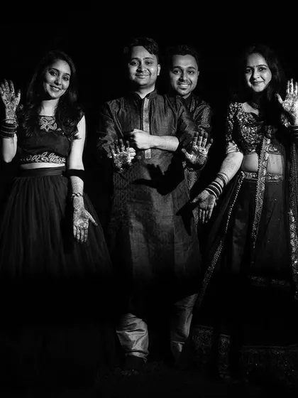 A creative black and white portrait of the groom with his family during the mehndi ceremony. The low-key lighting focuses on their happy faces and henna-adorned hands.