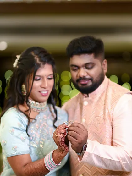 A candid shot of the couple admiring their rings together just after the exchange. The bokeh background of festive lights adds a magical feel to this happy moment.