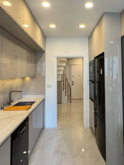 A view of a sleek parallel kitchen in Neeti Bagh, designed for maximum efficiency in a compact space. The glossy, light-colored cabinets and reflective flooring enhance the sense of space, while recessed ceiling lights provide ample illumination.