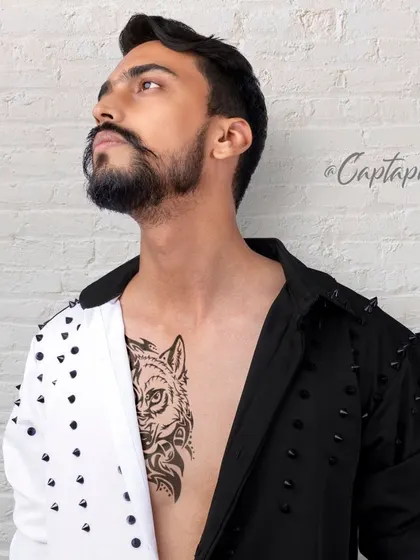 A stylish male fashion shot highlighting a unique two-tone shirt and chest tattoo. The upward glance and studio lighting create a confident and aspirational look suitable for fashion magazines.