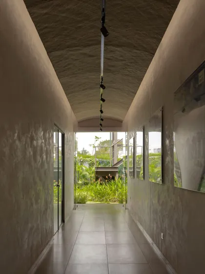 A vaulted corridor in the Brigade Oasis project, finished with lime plaster, creates a serene pathway. The passage frames a view of the lush green courtyard at its end, drawing nature into the building's core.