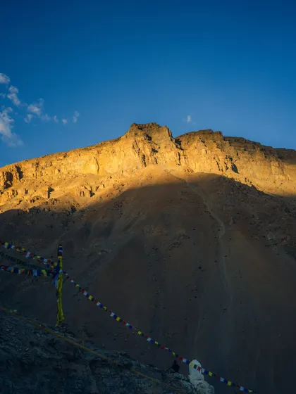 The golden hour light hitting the peak of a mountain in Spiti, with Tibetan prayer flags in the foreground. This shot combines natural beauty with cultural elements.