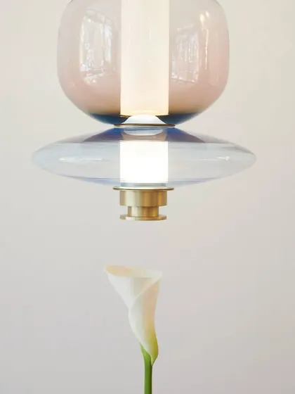 An artistic shot pairing a colorful Luna pendant with a delicate Calla lily, emphasizing the light's sculptural and organic qualities.