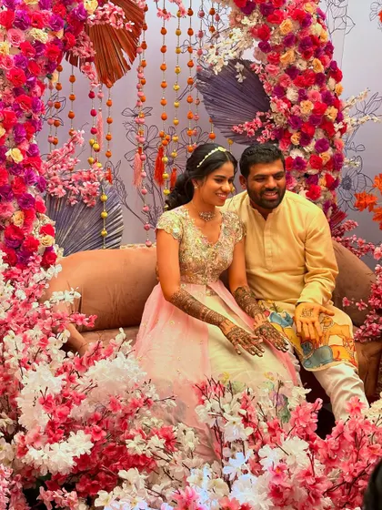 A happy couple seated amidst a beautiful cherry blossom themed decor for their mehndi ceremony.