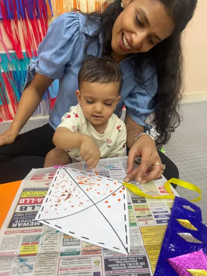 A mother and child work together on a kite craft, using their fingers to apply decorations, which is a great sensory activity.