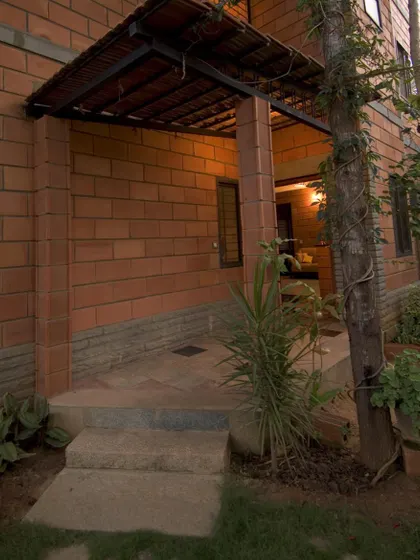 The entrance portico of the Sharada Residence features exposed brick pillars and a tiled roof. This detail provides a sheltered, welcoming entry point that introduces the home's core material palette.