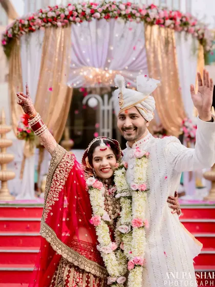 Pure celebration. The newly married couple waves joyfully, with the bride's hand raised in excitement, capturing the peak emotion of their wedding day.