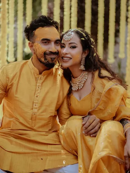 A sweet, candid moment with the bride leaning in towards her groom, both covered in turmeric paste. It's a beautiful image of love and playfulness.