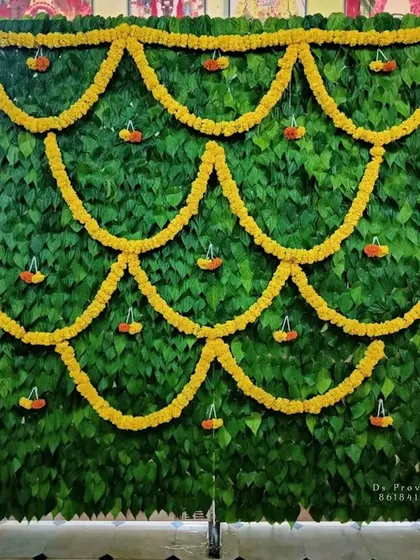 This unique and eco-friendly backdrop is made entirely of fresh betel leaves, accented with marigold flower garlands. It's a beautiful and fragrant option for an ear piercing ceremony or other traditional functions.