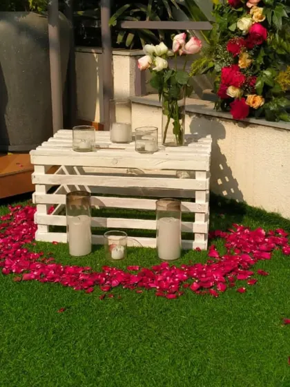 A close-up of the romantic decor, featuring a heart made of rose petals on the grass, surrounded by candles in glass holders.