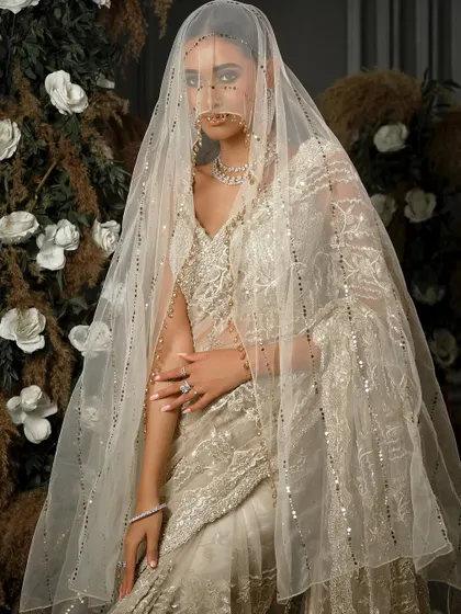 A magazine-style shot featuring a veiled bride. The Nitika Gujral saree and the sheer veil create a high-fashion, editorial look that is both mysterious and captivating.