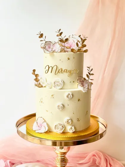 An elegant two-tiered cake with delicate, wafer-paper flowers and golden leaves. The simple design and gold splatter give it a sophisticated and modern feel.
