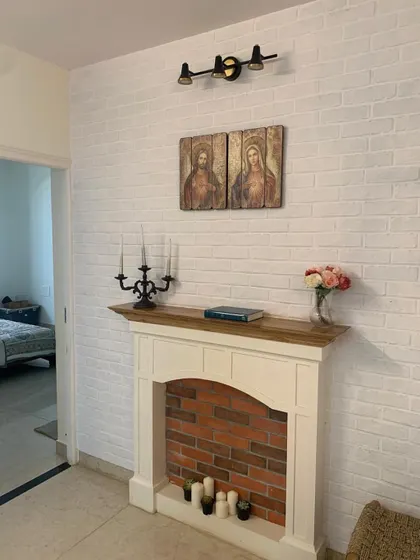 A fireplace so good, you’ll want to fake winter just to light a scented candle and feel something. A cozy, faux fireplace with a white brick-patterned wall.