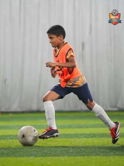 A player in an orange bib dribbles forward during a practice match, applying his skills in a game situation.