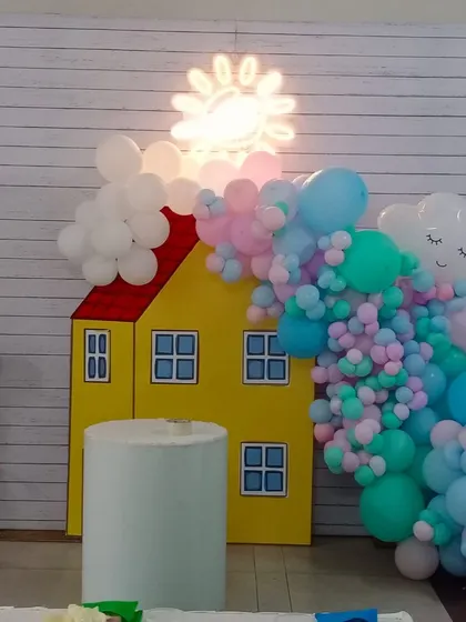 A cute Peppa Pig theme, with a prop of Peppa's house and a pastel colored balloon garland representing clouds and the sun.