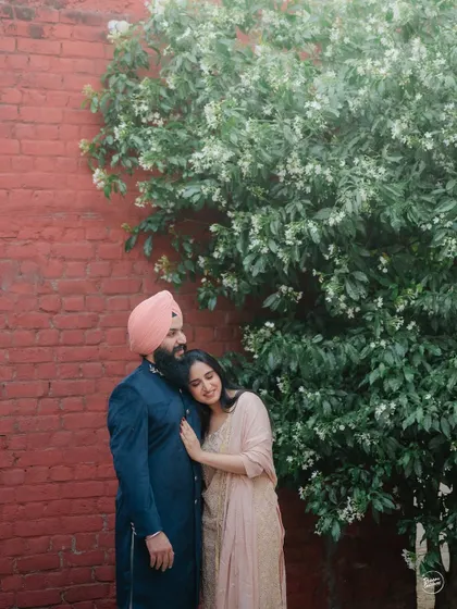 A tender embrace against a rustic wall, framed by a flowering tree. This shot from their Amritsar pre-wedding session is a perfect blend of rustic charm and natural beauty.