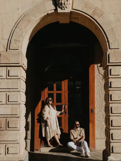 A beautifully composed shot of a couple framed by a grand stone archway in Mumbai. The warm sunlight creates a dramatic shadow, adding a touch of old-world charm and romance to the scene.