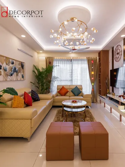 This living room is a perfect blend of warmth and vibrancy. A neutral sofa is accented with colorful pillows and ottomans, while a statement chandelier and a large plant add life and character to the room.