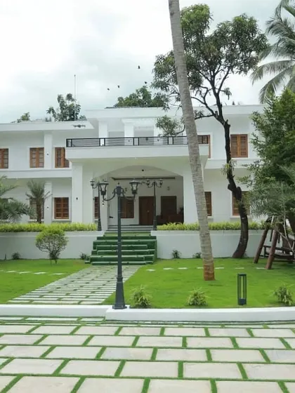 The front view of a large residence, showcasing the balance between hardscape and softscape. The stone paver driveway is softened by a large lawn, mature palm trees, and strategically placed lampposts that guide visitors to the entrance.
