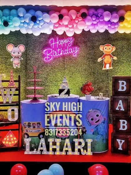 A Cocomelon party for Lahari's second birthday, set against a grass wall with a neon "Happy Birthday" sign for a modern twist on the popular theme.