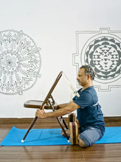 Using a chair and strap in Baddha Konasana (Bound Angle Pose) helps maintain an upright posture while gently opening the hips, demonstrating our focus on prop-based alignment.