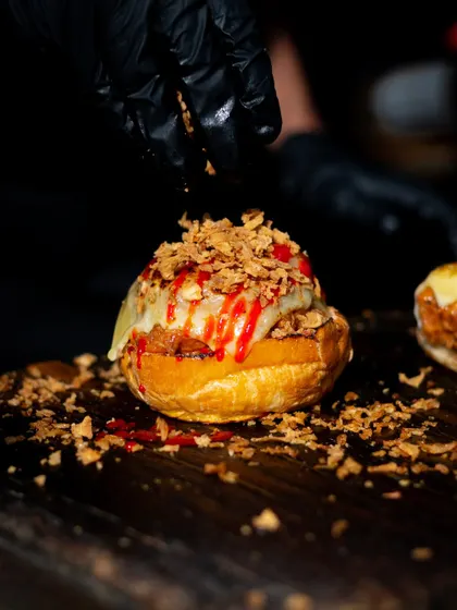 The final touch of crispy onions being sprinkled onto a pulled pork bagel. This image focuses on the texture and generosity of the topping.