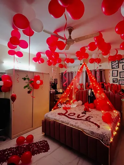 A full view of the room with a lit canopy, ceiling balloons, and rose petal art on the bed. This style is perfect for creating a cozy and intimate celebration space.