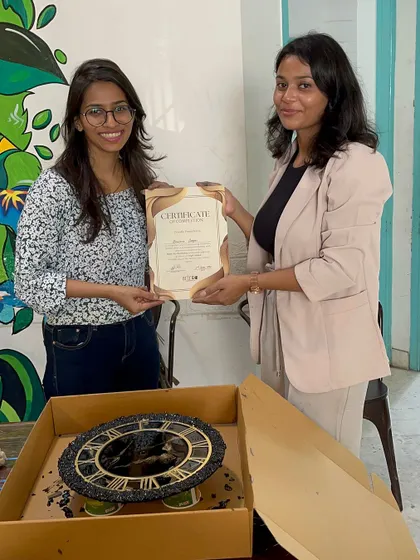 A participant receives her certificate of completion at our resin art workshop, proudly standing by her finished marble technique clock.