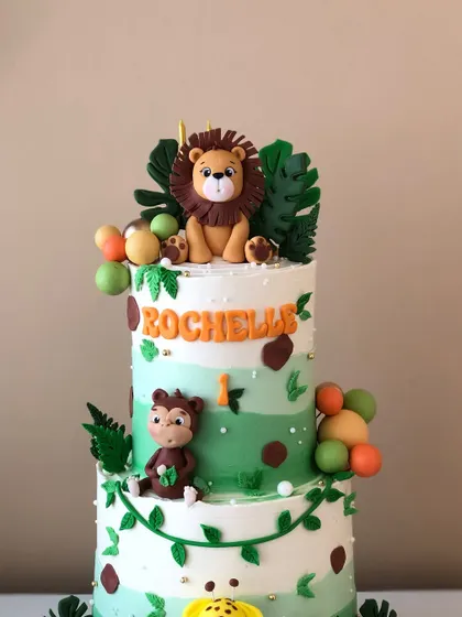 The top tier of the safari cake, featuring a cute lion and tropical leaves.
