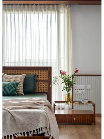 The master suite in 'Vasudhalayah' is a peaceful haven with sunlit French windows and our signature wooden ledges. The fluted bedside table and cane headboard add texture and classical flair.