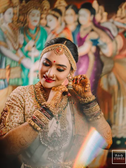 A beautiful close-up of the bride adjusting her intricate jhumka earring, showcasing the details of her jewelry and henna.