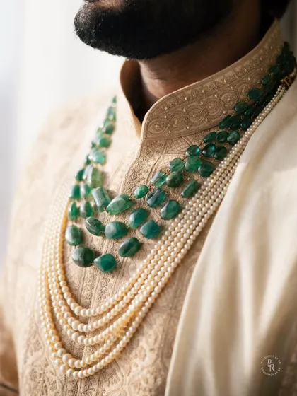A close-up of the groom's multi-layered pearl and emerald necklace, a statement piece of jewelry for his wedding day.