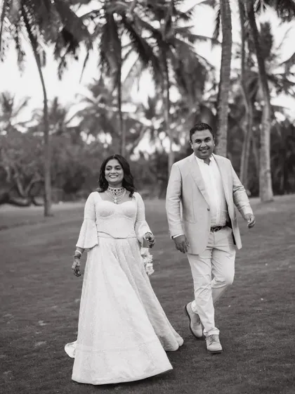 A classic black and white shot of a couple walking through the palm-fringed lawns of their Goa wedding venue.