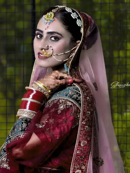 A striking bridal portrait with dramatic lighting. The focus is on the bride's expressive eyes and the intricate details of her nath (nose ring) and other traditional jewelry.