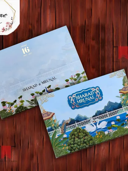 A picturesque wedding invitation featuring a beautiful landscape of mountains and a lake with swans, framed by traditional Indian architectural elements.