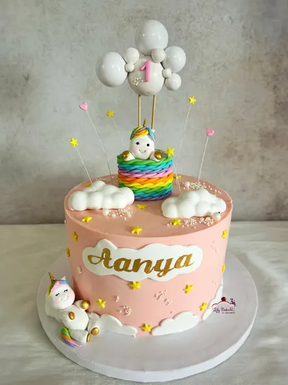 A magical unicorn-themed first birthday cake, with a unicorn in a hot air balloon and another one sleeping on a cloud.