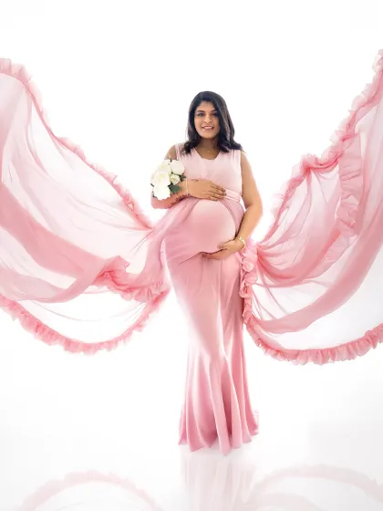 A beautiful solo portrait of a mother-to-be in a flowing pink maternity gown, creating a dynamic and angelic look against a clean white background. This style is perfect for celebrating the beauty of pregnancy.