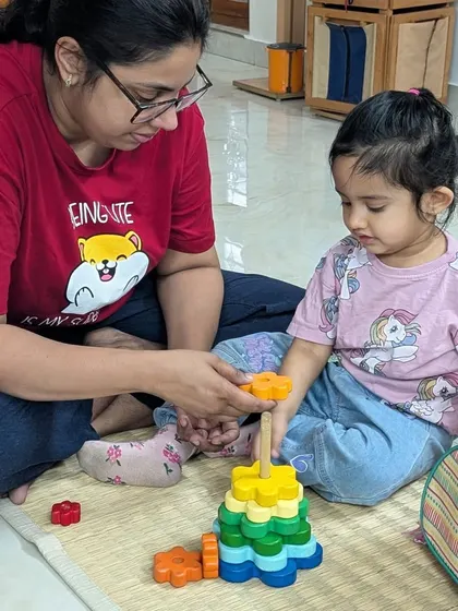 A mother and daughter work together on a colorful flower stacking toy. This shared activity during the settling-in period makes the new environment feel safe and familiar.